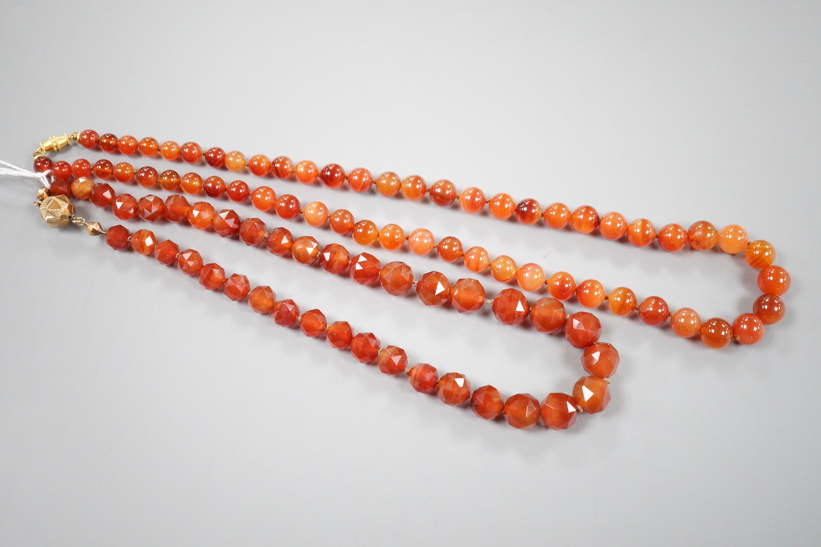 Two single strand carnelian necklace, one with facet cut beads, 44cm & 60cm, both with yellow metal clasps.